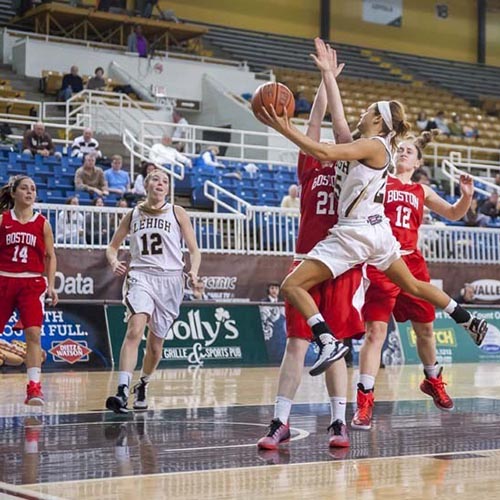 Kayla Burton is mid-air, lifting a basketball toward the net as defenders raise their arms.
