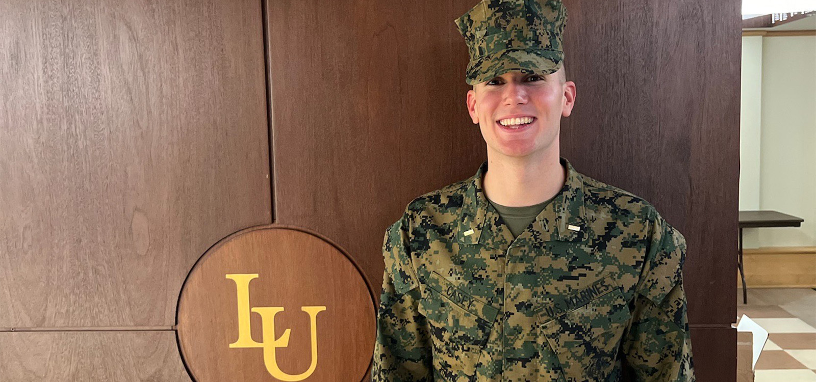 Keagan Casey wears his Army fatigues and stands next to a Lehigh logo.