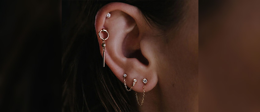 Close up of an ear with different gold and diamond stud earrings.