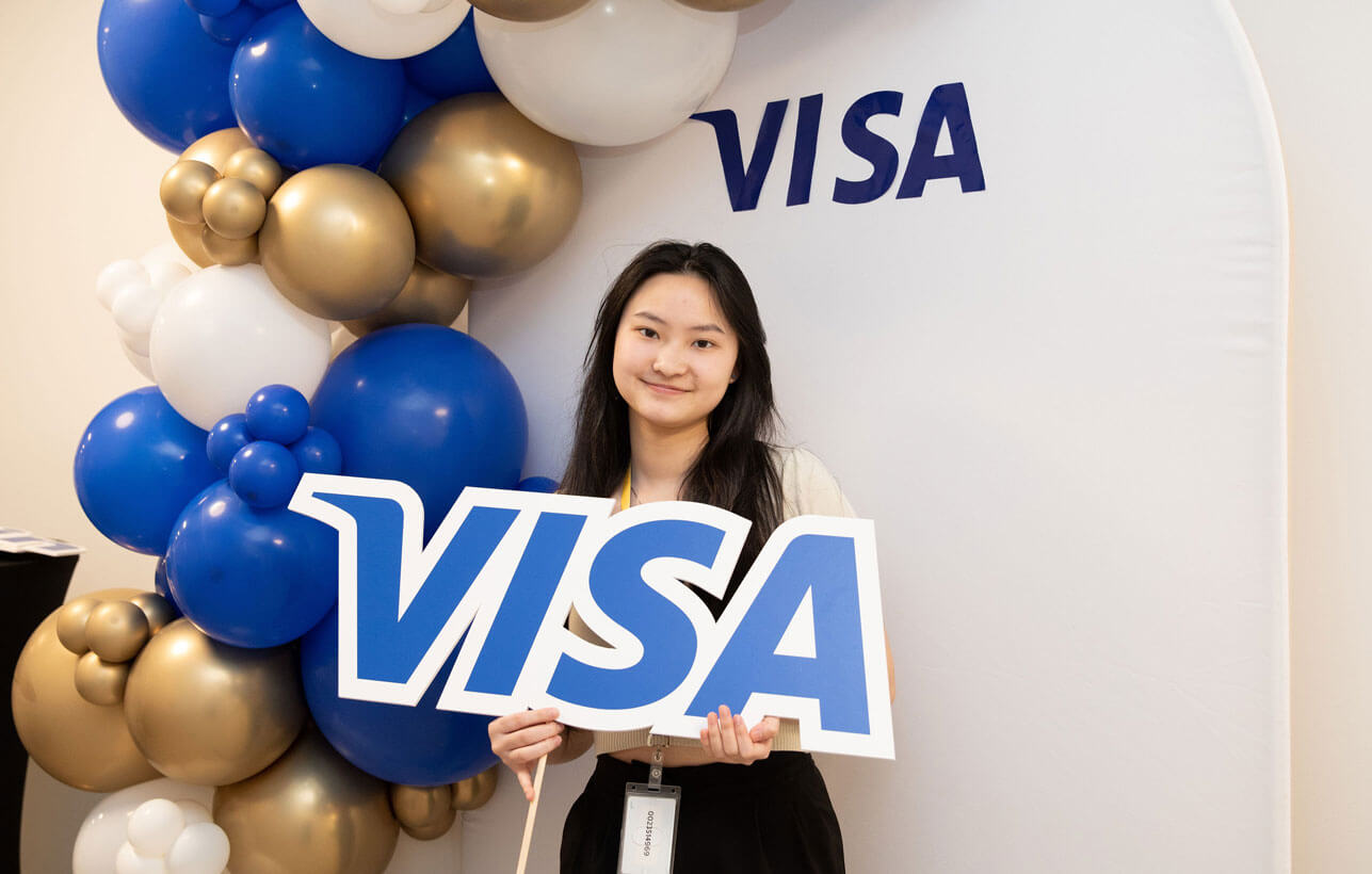 Kelly Chen posing with the Visa logo under a blue and white balloon arch