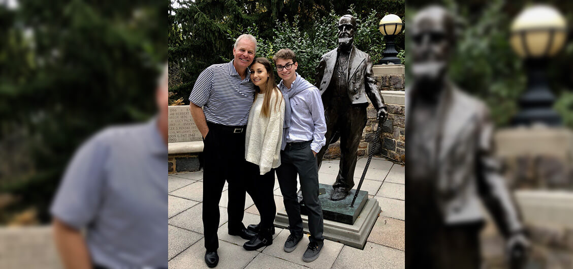 A family of three pose closely together, smiling, next to a bronze Asa Packer statue on the Lehigh campus