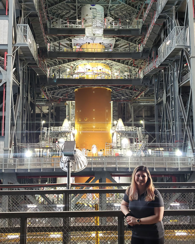 Kristina Gonzalez standing along a platform with the Artemis I Vehicle Assembly behind her