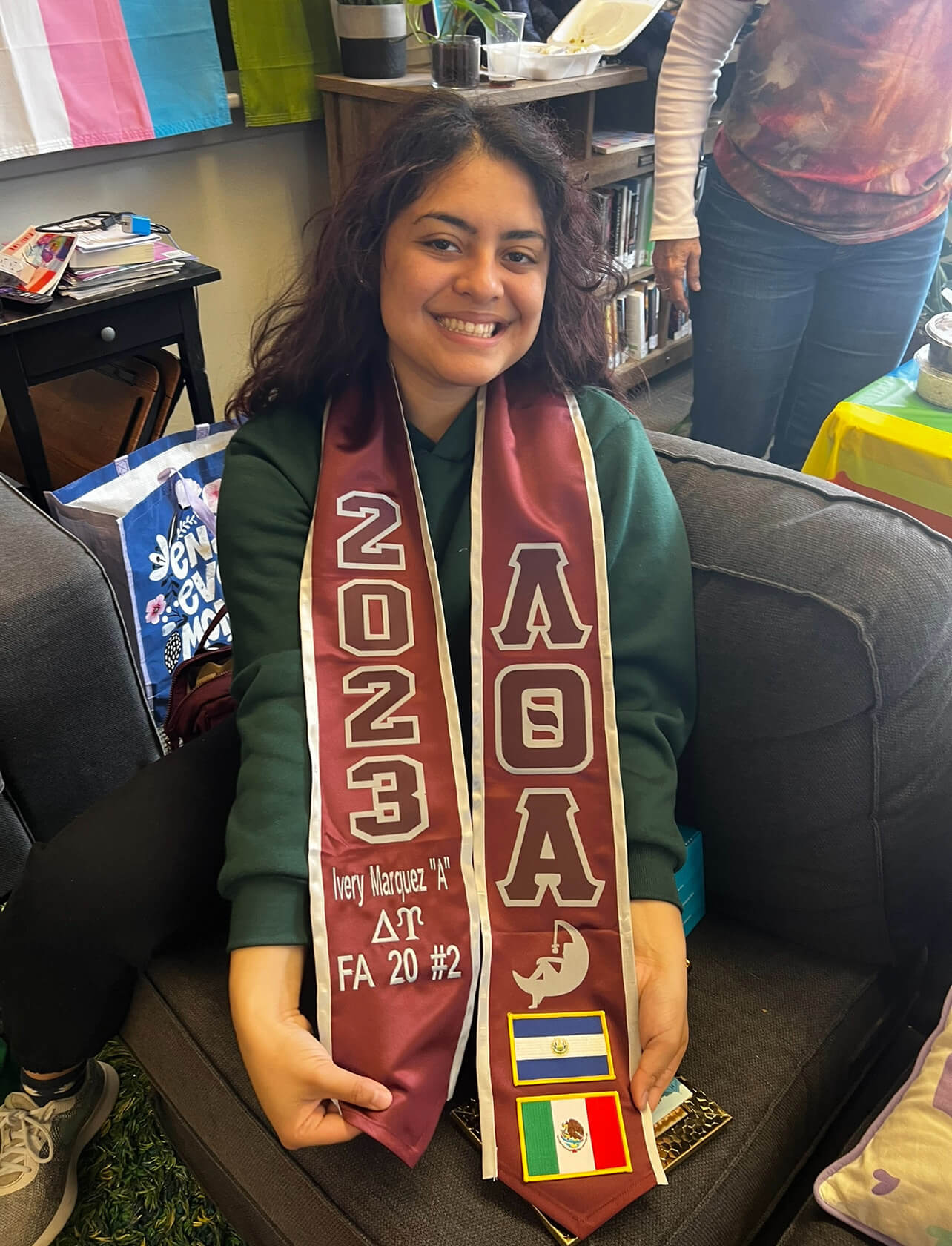 Student sits at the Pride Center wearing sorority sash with a smile.