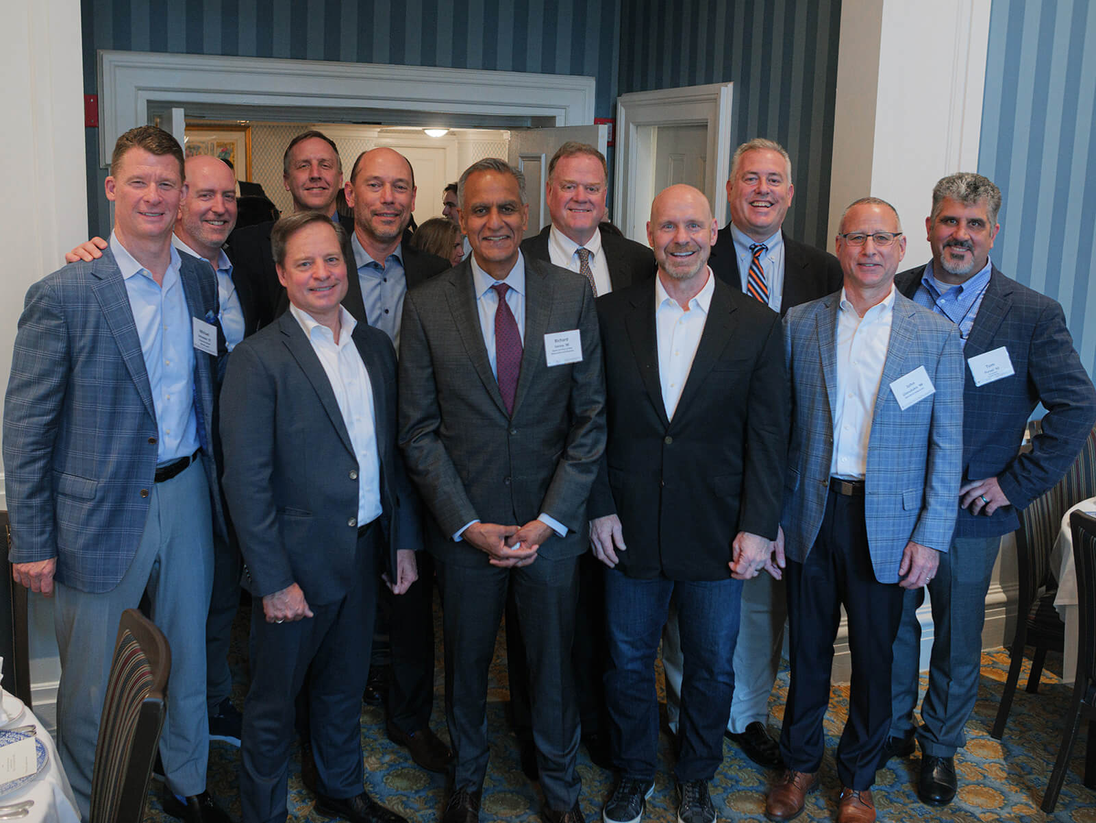 Richard Verma stands in the center position of a posed photo with a group of male alumni, all wearing suits or blazers.