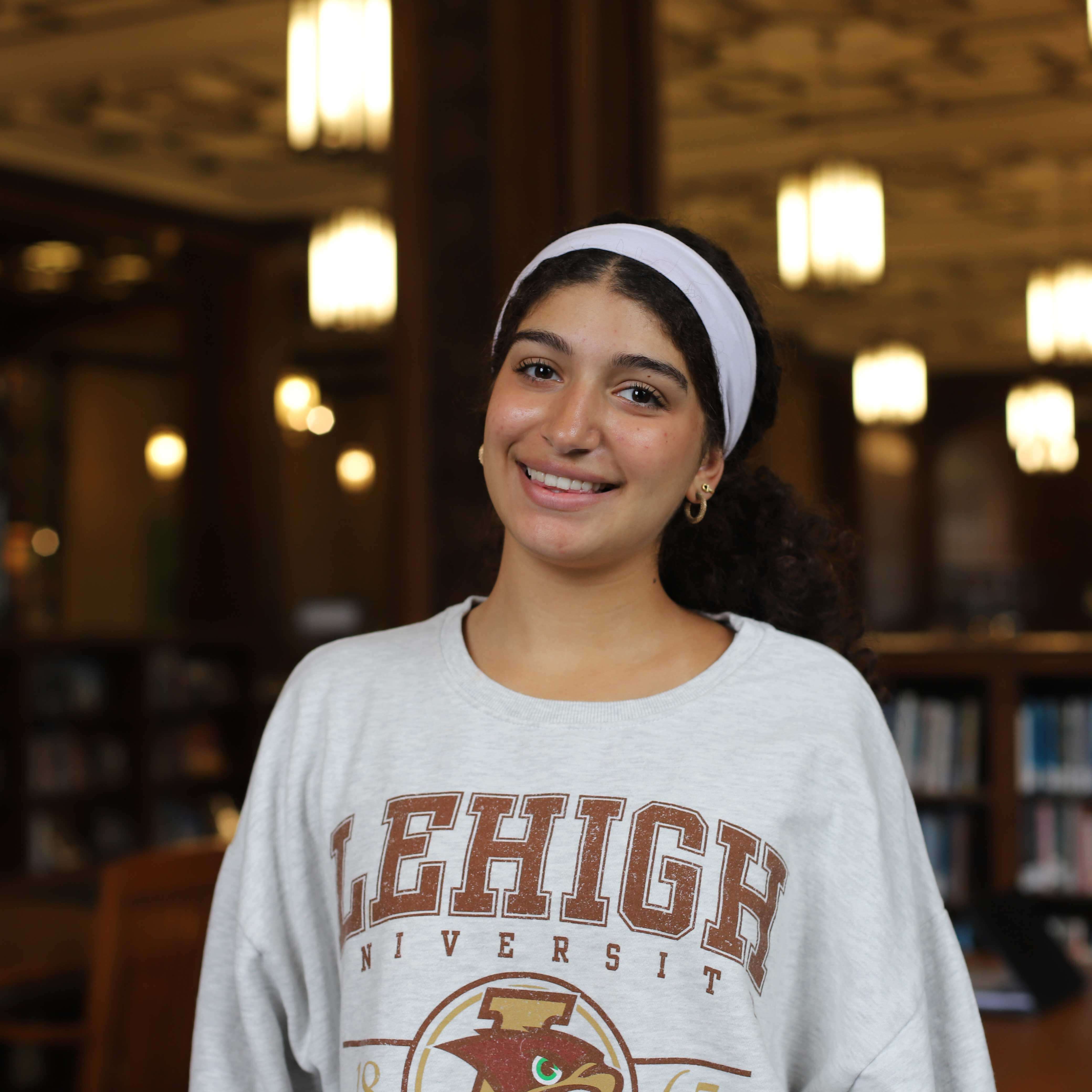 Laura wears a grey Lehigh sweatshirt and a white headband. Linderman Library is visible behind her.