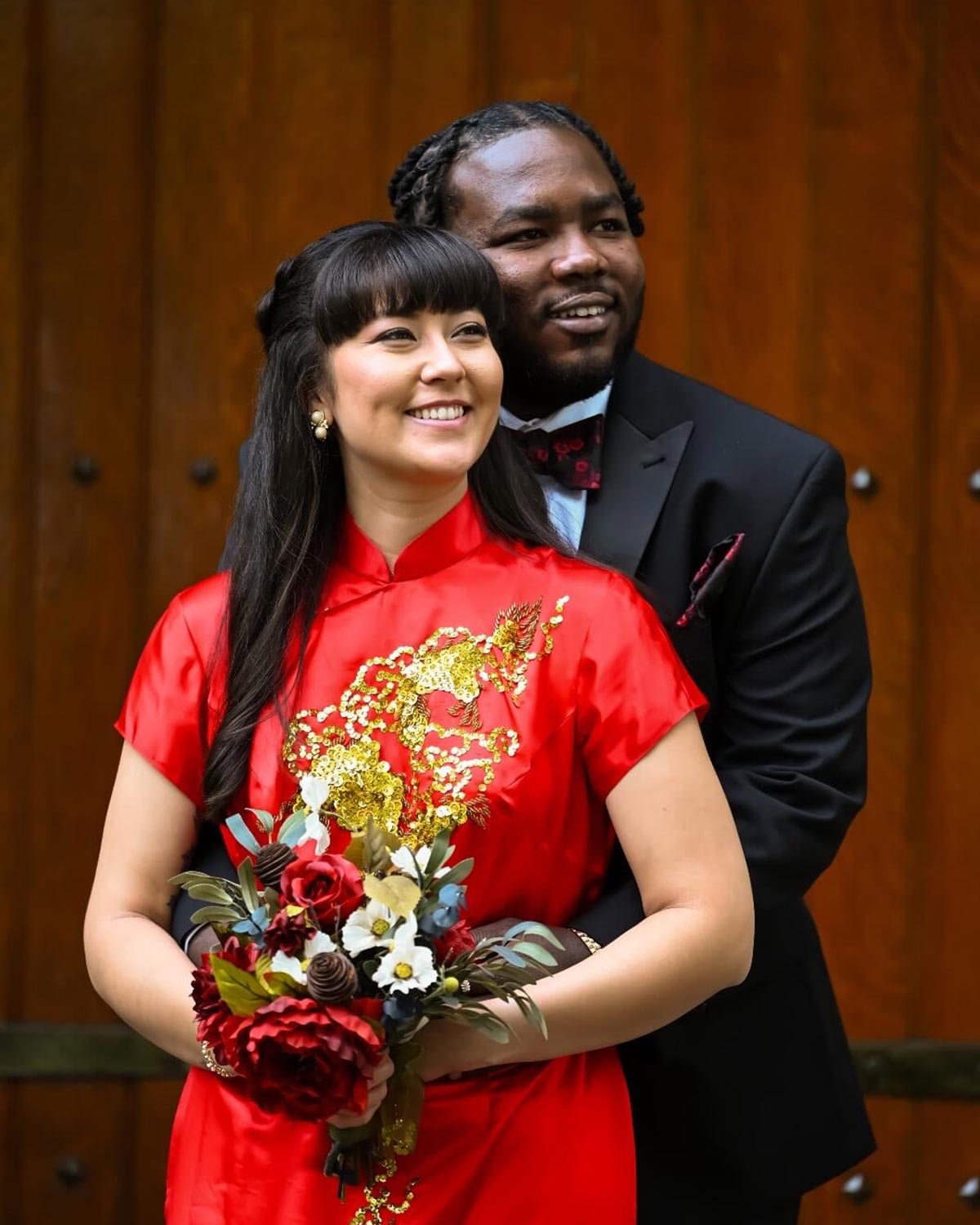 Lauren and Francis pose after their wedding; she wears a red, kimono-style dress and he wears a black suit.