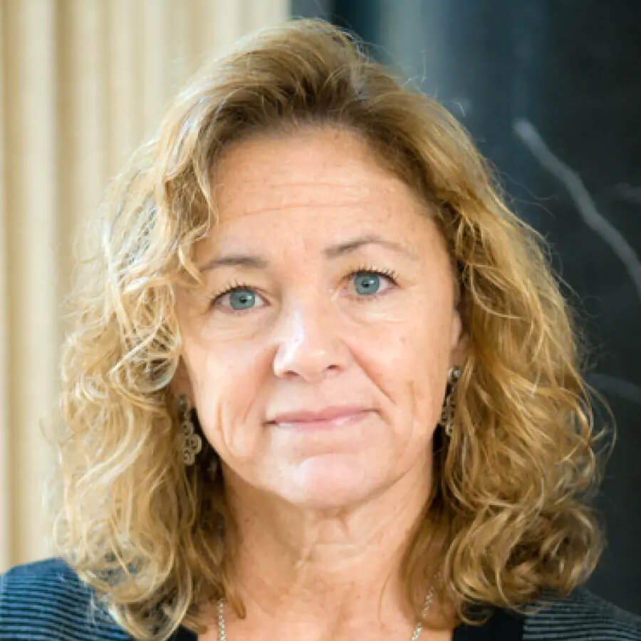 Headshot of a female posed with a closed mouth smile and blonde curly hair, blue eyes, and drop earrings.