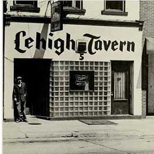 A black and white photo of the Lehigh Tavern circa 1960s. The name of the bar is written above the entrance; a man stands outside.