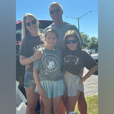 Jessica and Jason stand with their two children in a parking lot before a Rivalry game. Two of them wear Lehigh merch.