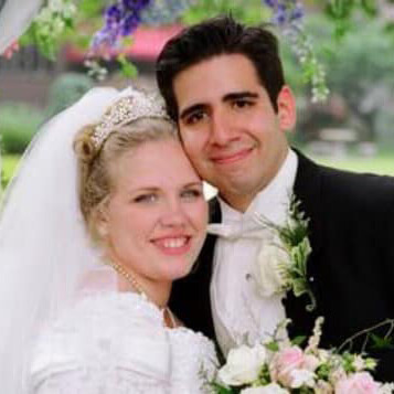 Bride and groom stand cheek to cheek while posing against a garden backdrop.