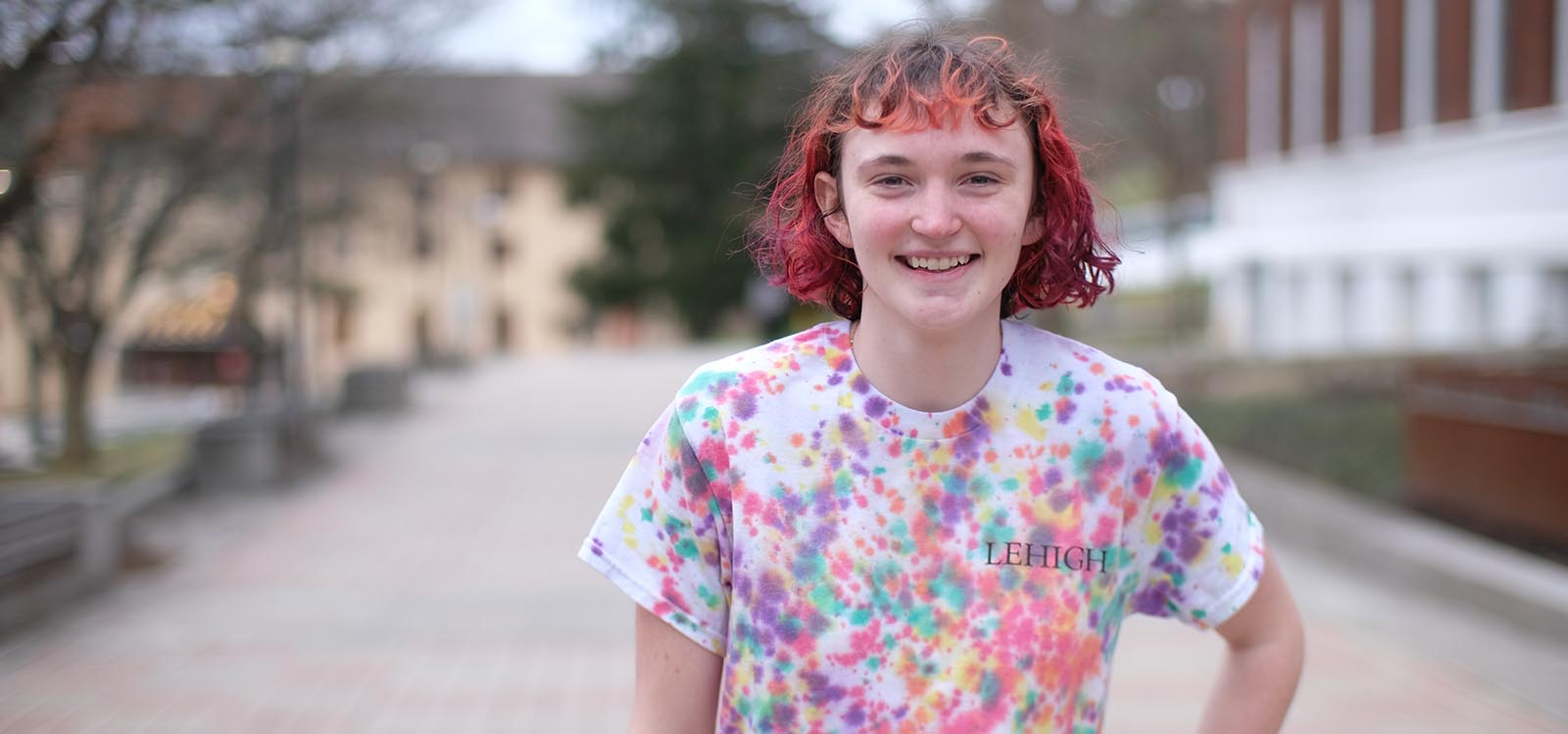 Lily Paschke '27 wears a tie dye Lehigh T shirt and stands on campus near Williams Hall