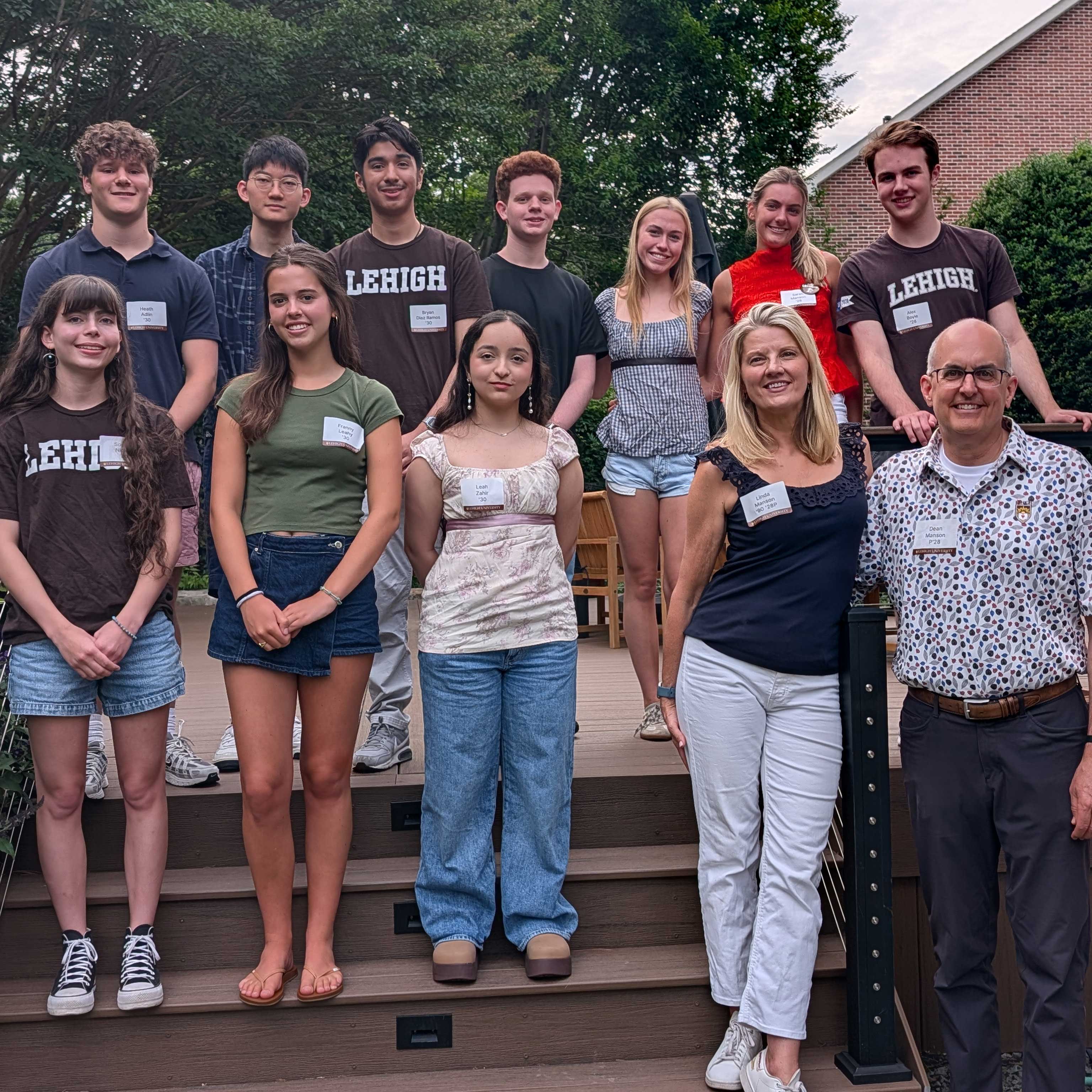 A group of students stand together at a Sendoff and smile; some wear Lehigh merch. Linda and her husband stand beside them.