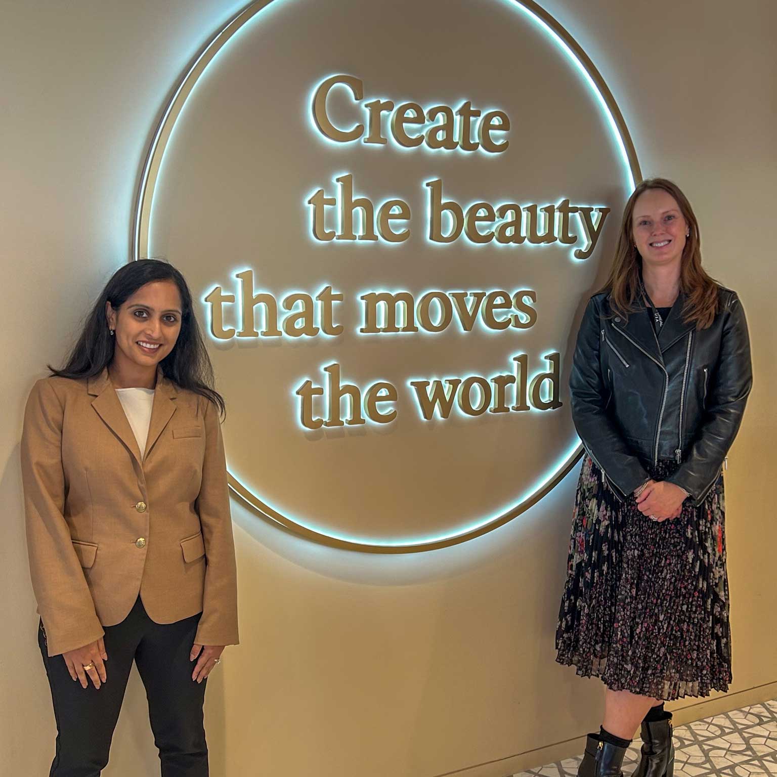 Two Lehigh alumni stand on either side of a sign that reads 'Create the beauty that moves the world' and smile. 