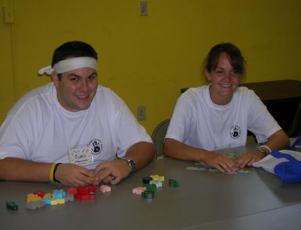 A male student wearing a white headband sits at a table with a female student, both handling puzzle pieces.