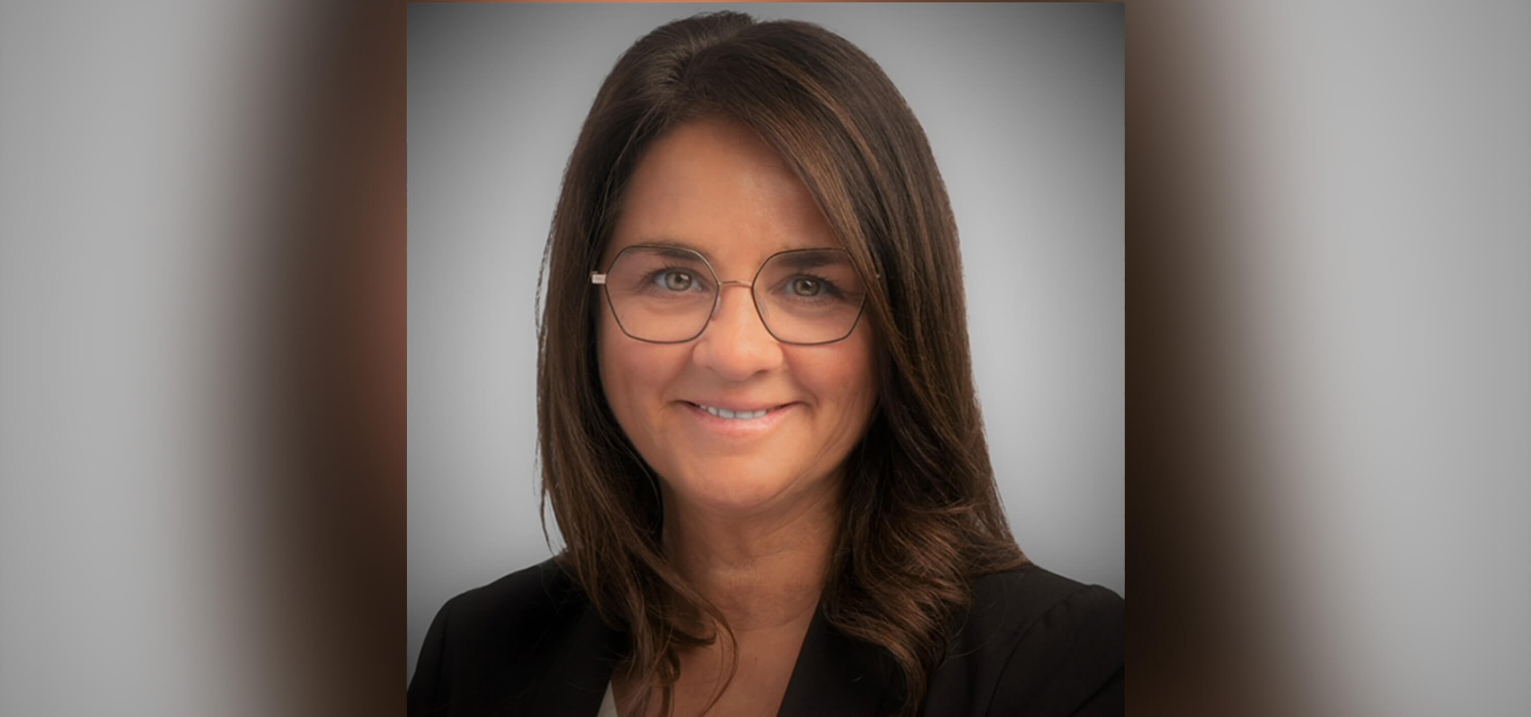 Female wearing glasses and a black blazer over a white shirt poses and smiles for a headshot.