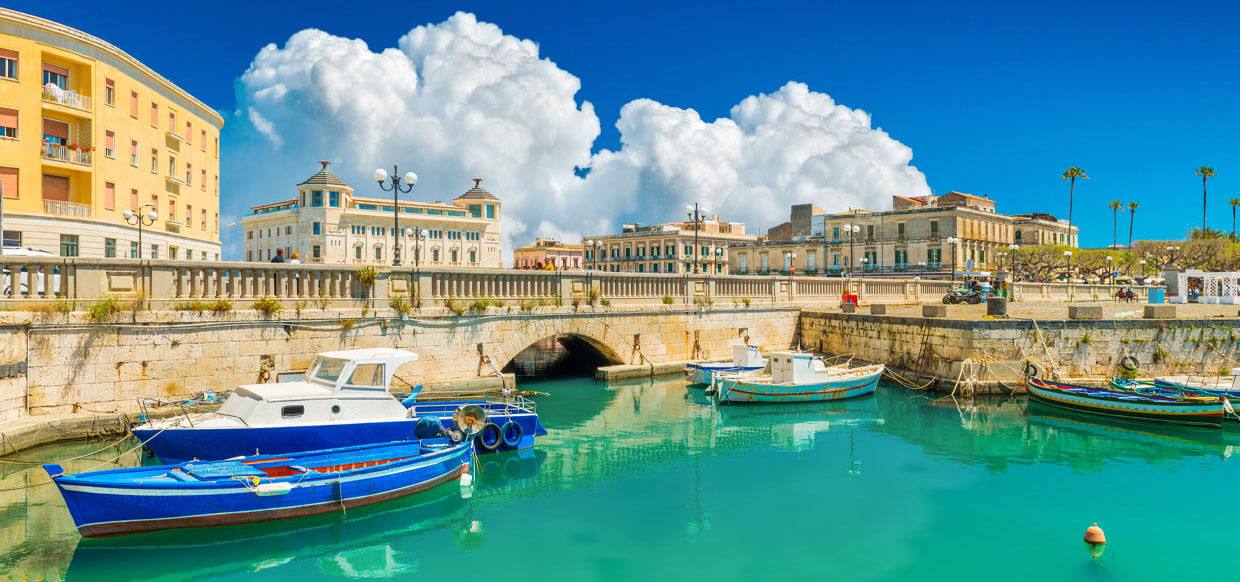 A bright bl;ue waterway containing fishing boats and surrounded by stone buildings.