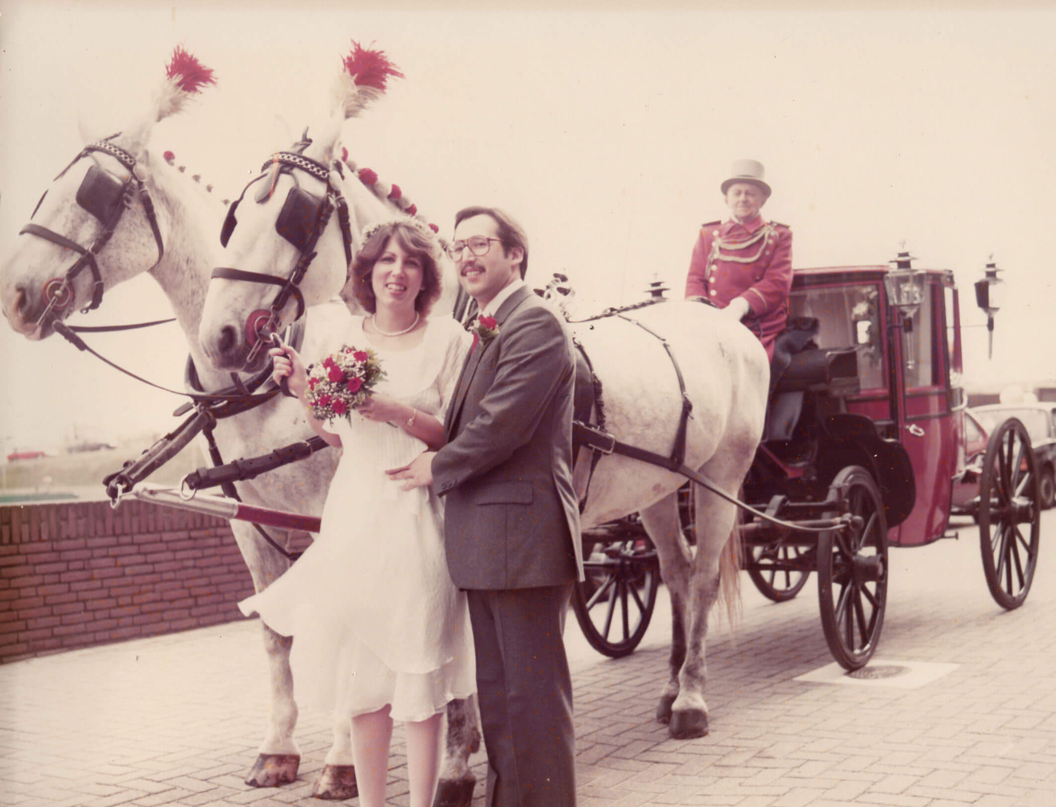 Susan and Mark Hembarsky posing in front of a red horse drawn carriage on their wedding day.