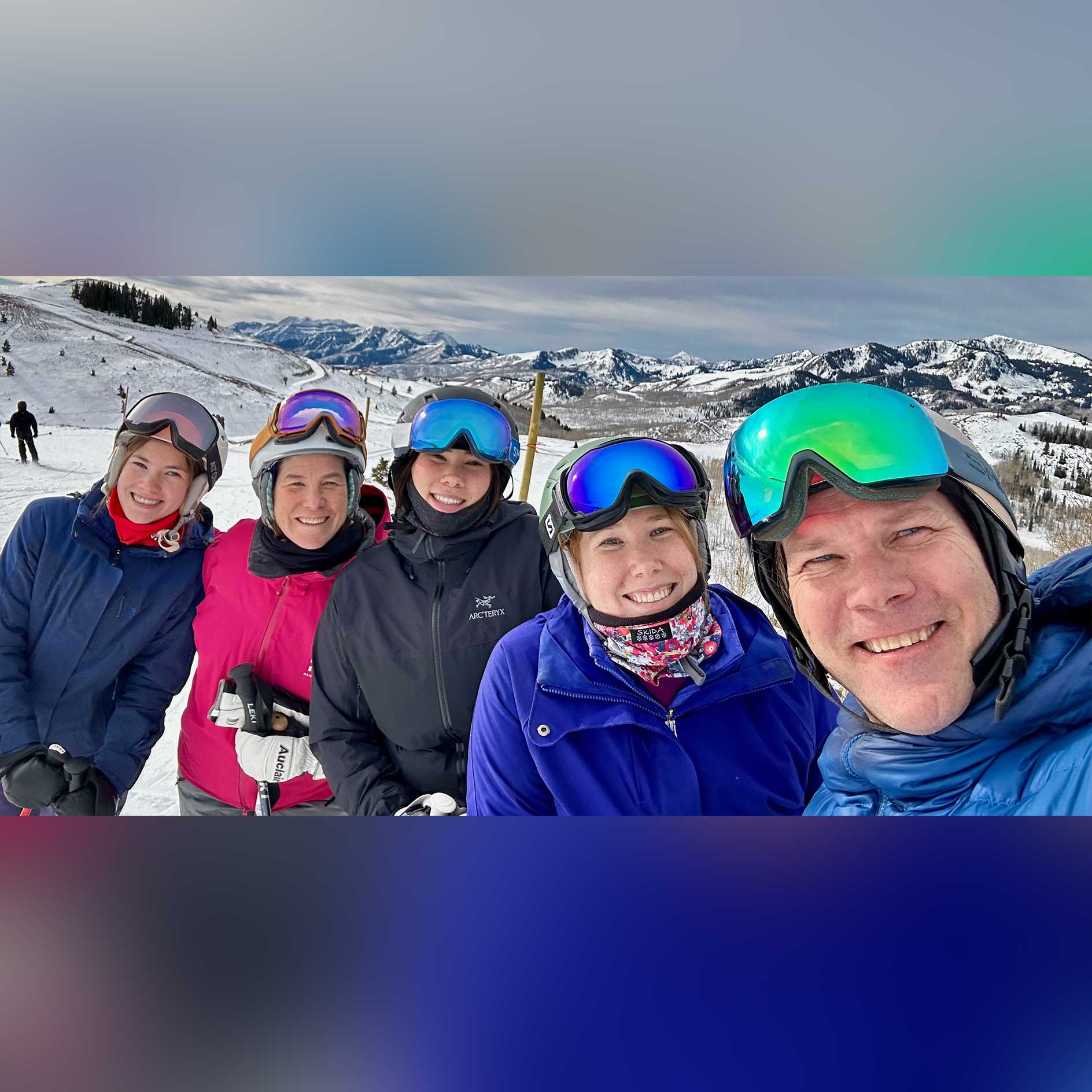 Chris and his family pose together on a mountain while skiing. They wear thick clothing and goggles.