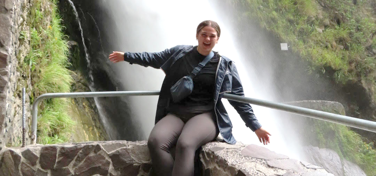 McKenna sits on a ledge in front of a waterfall in Ecuador