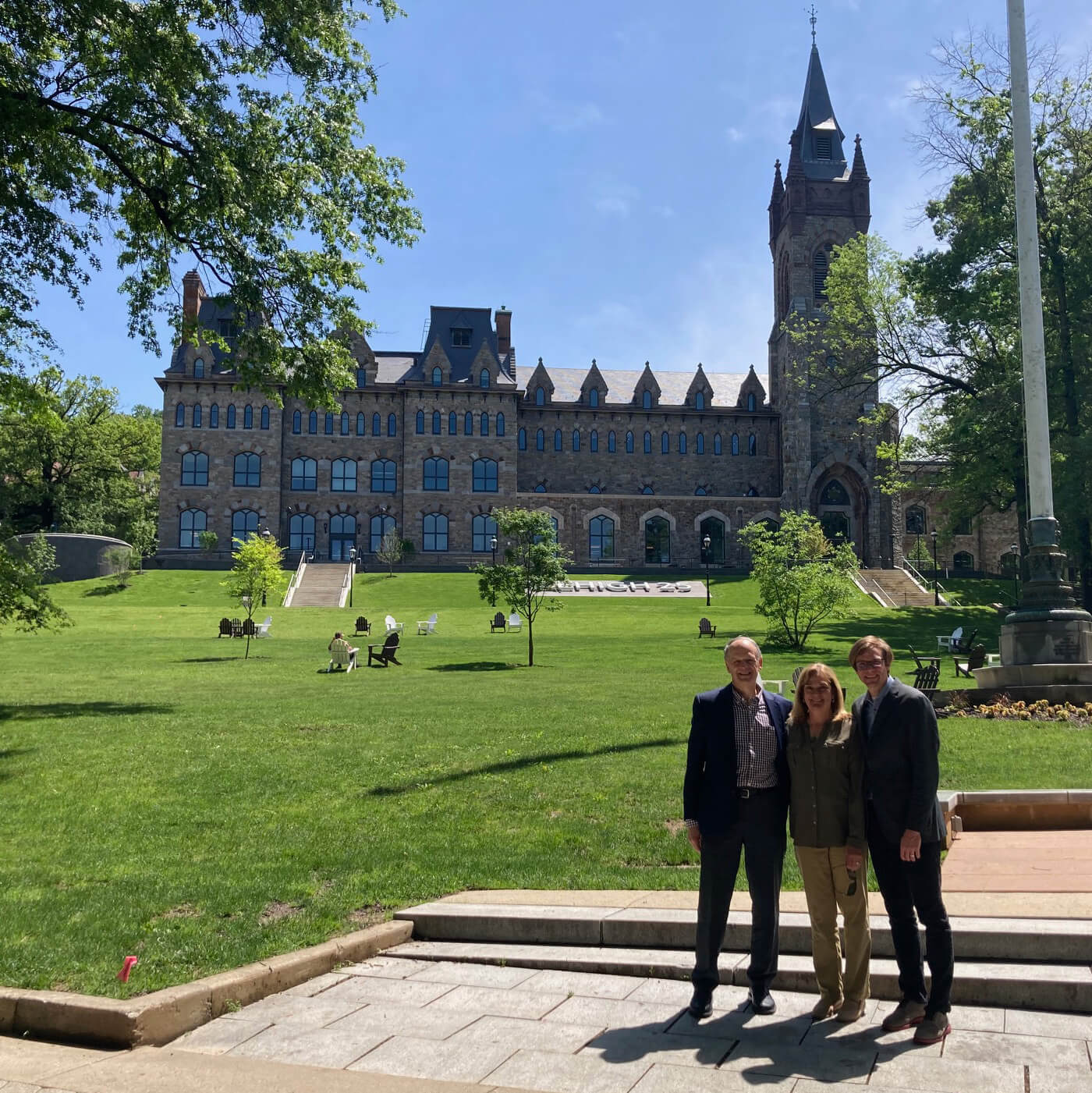 Chris and Colin pose, wearing sport jackets, with their mother Elaine between them with the Clayton University Center and the flag pole shown behind them.