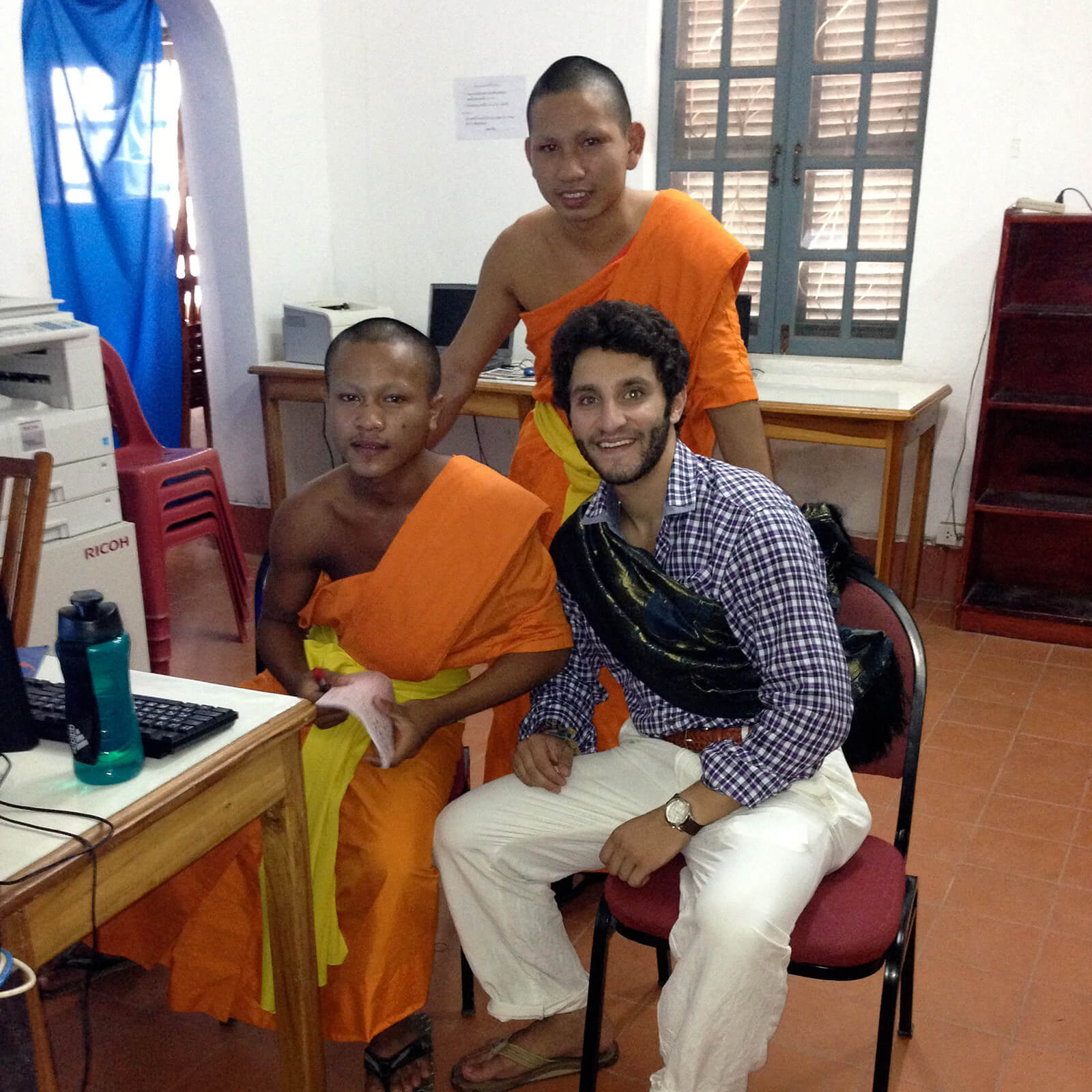Michael Langer sits at a computer with two Laos locals, all smiling for the camera.