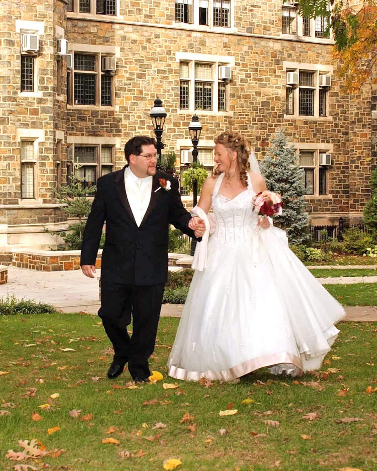 Michael and Moe walk across campus after their wedding; Moe wears a long, ballroom wedding dress and Michael wears a black suit.