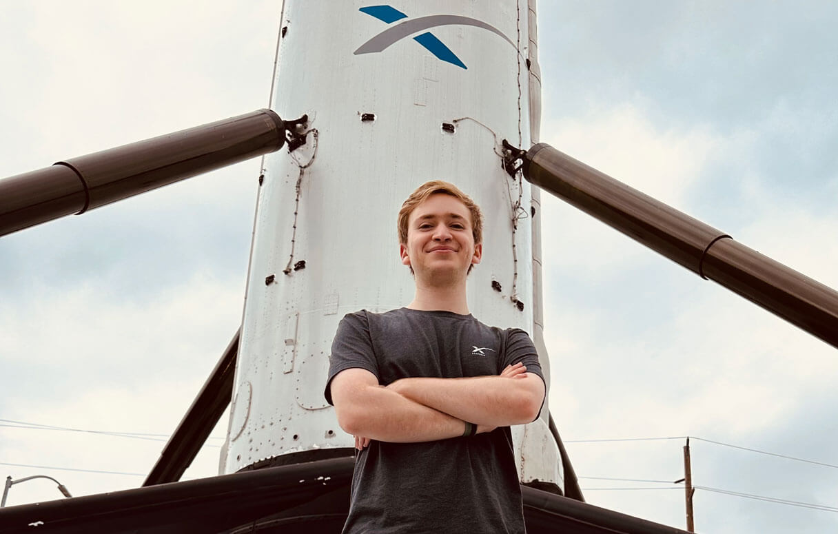 Michael Baron standing with arms crossed in front of a Space X rocket