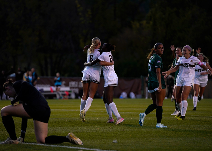 Two players embrace on the pitch as others run over to celebrate a goal