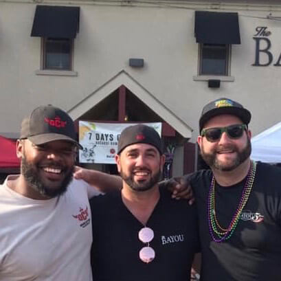 Mo Taylor, Cristian Duarte, and Jerry Straub smiling together in front of The Bayou, the flagship restaurant they co-own.