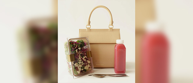 Tan bag with boxed salad, silver cutlery, and pink drink bottle in front of it.