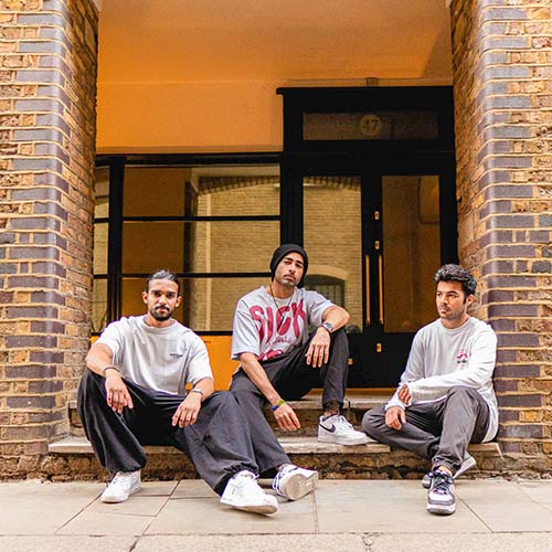 Aakash Phulwani sits outside in the center of a brick doorway with two founders of his dance crew