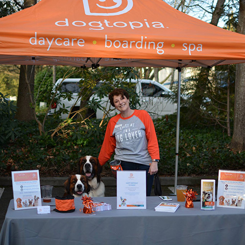 Woman and two dogs stand below a tent marking Dogtopia