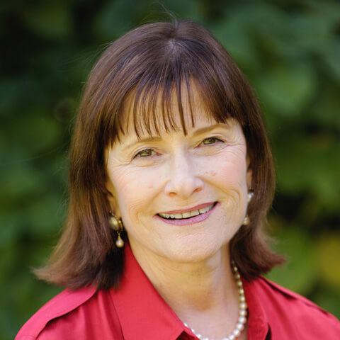 Nancy Berman shown from her shoulders up, smiling for a headshot and wearing a red collared blouse and pearls.