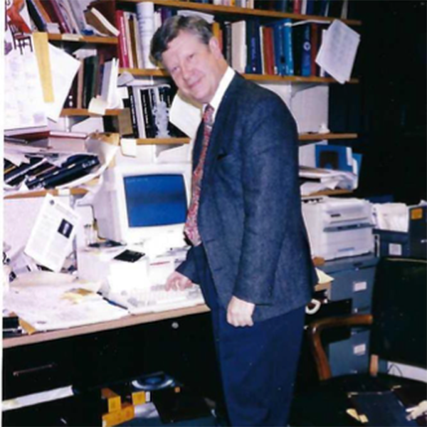 Ned Heindel stands at a messy desk and office.