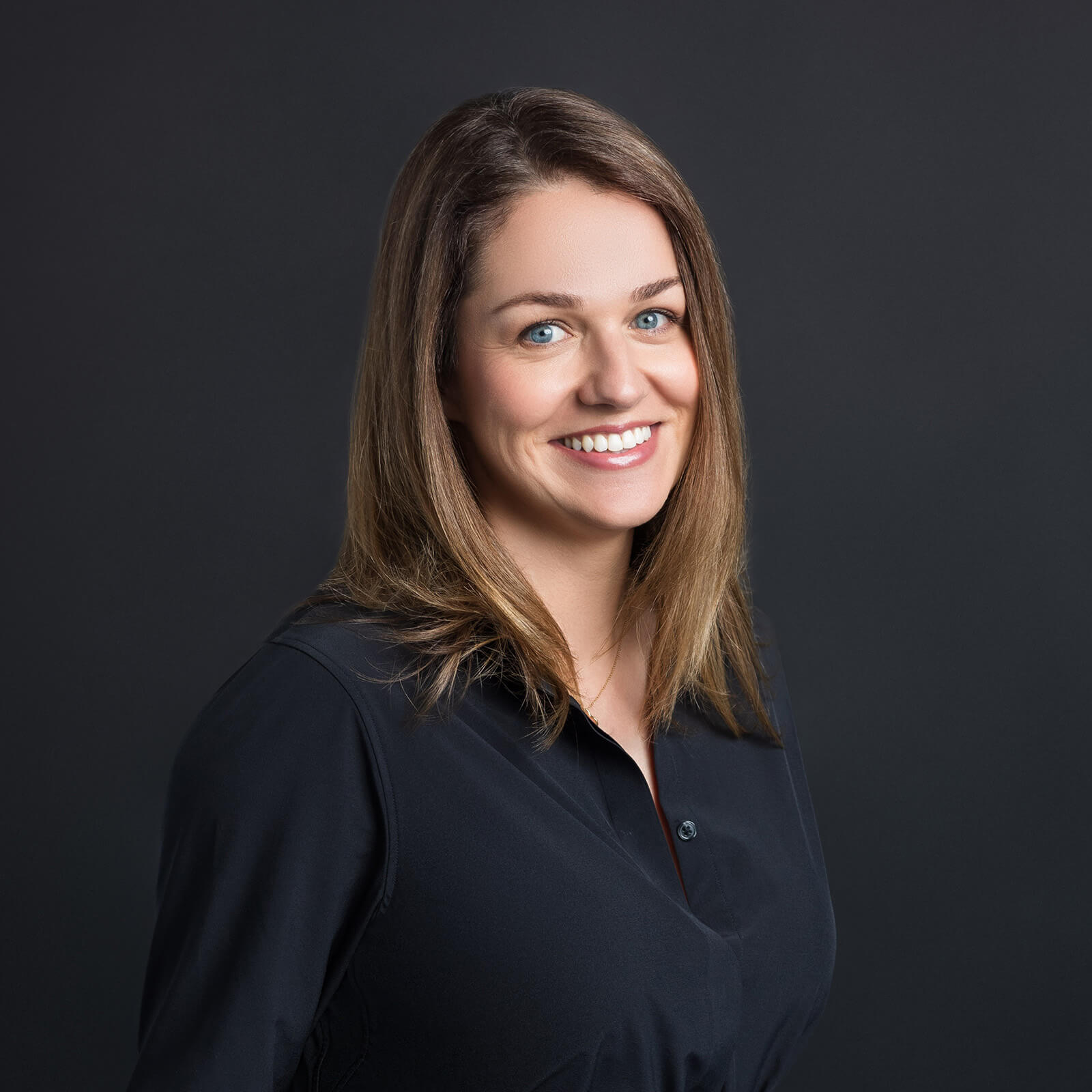 Nicole Ganot poses against a dark gray background smiling and wearing a black collared blouse.