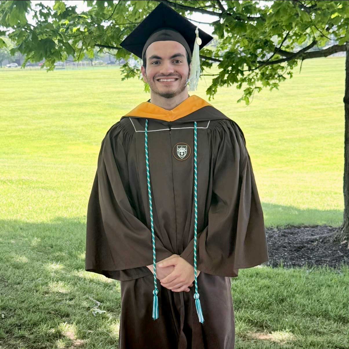 Nikolas wears his cap and gown while smiling outside on graduation.