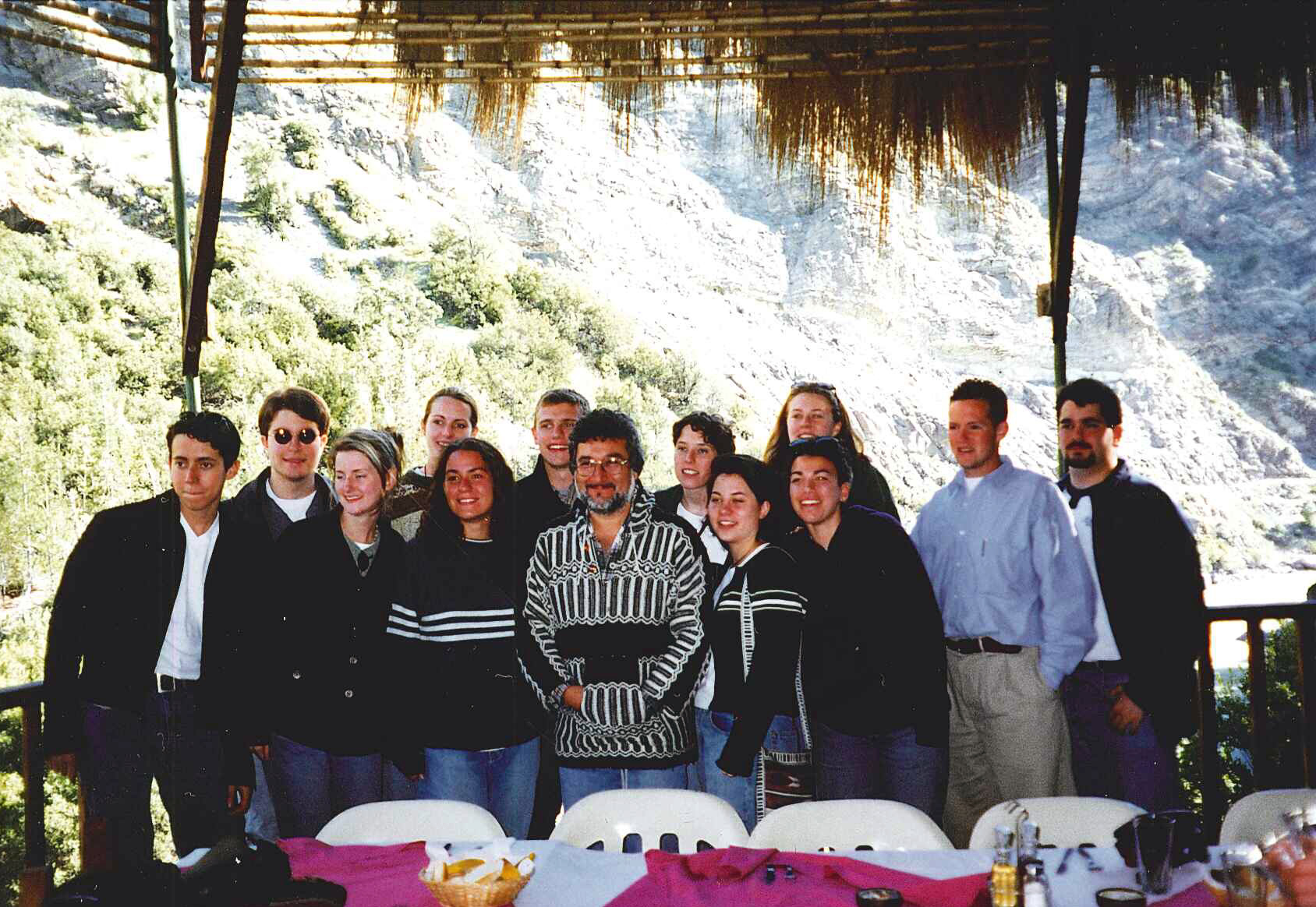 Louis and his classmates pose and smile; the landscape is a lush green behind them. Louis is on the far left in a black jacket.