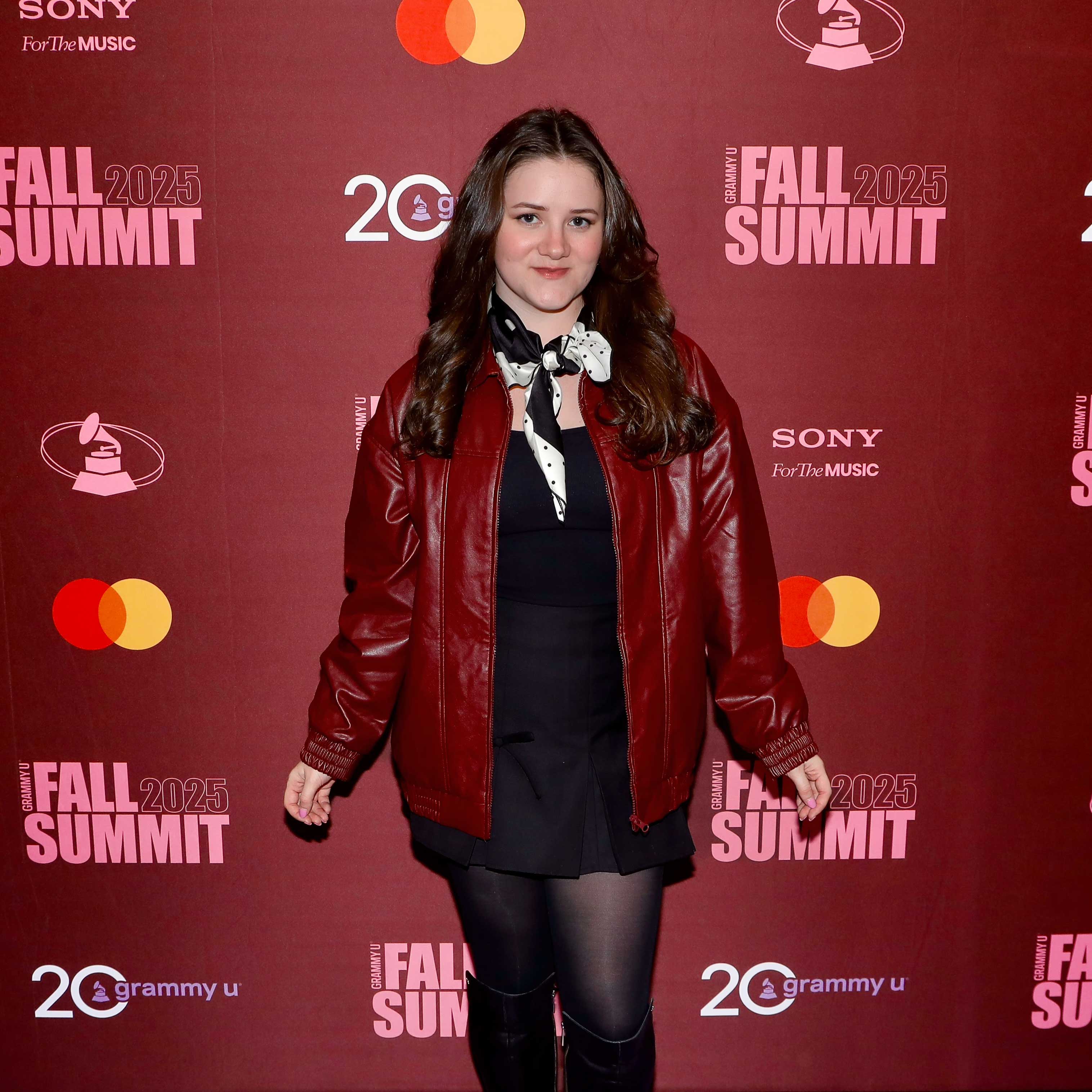 Olivia White standing before a red step and repeat for the Grammy U Fall Summit 2025.