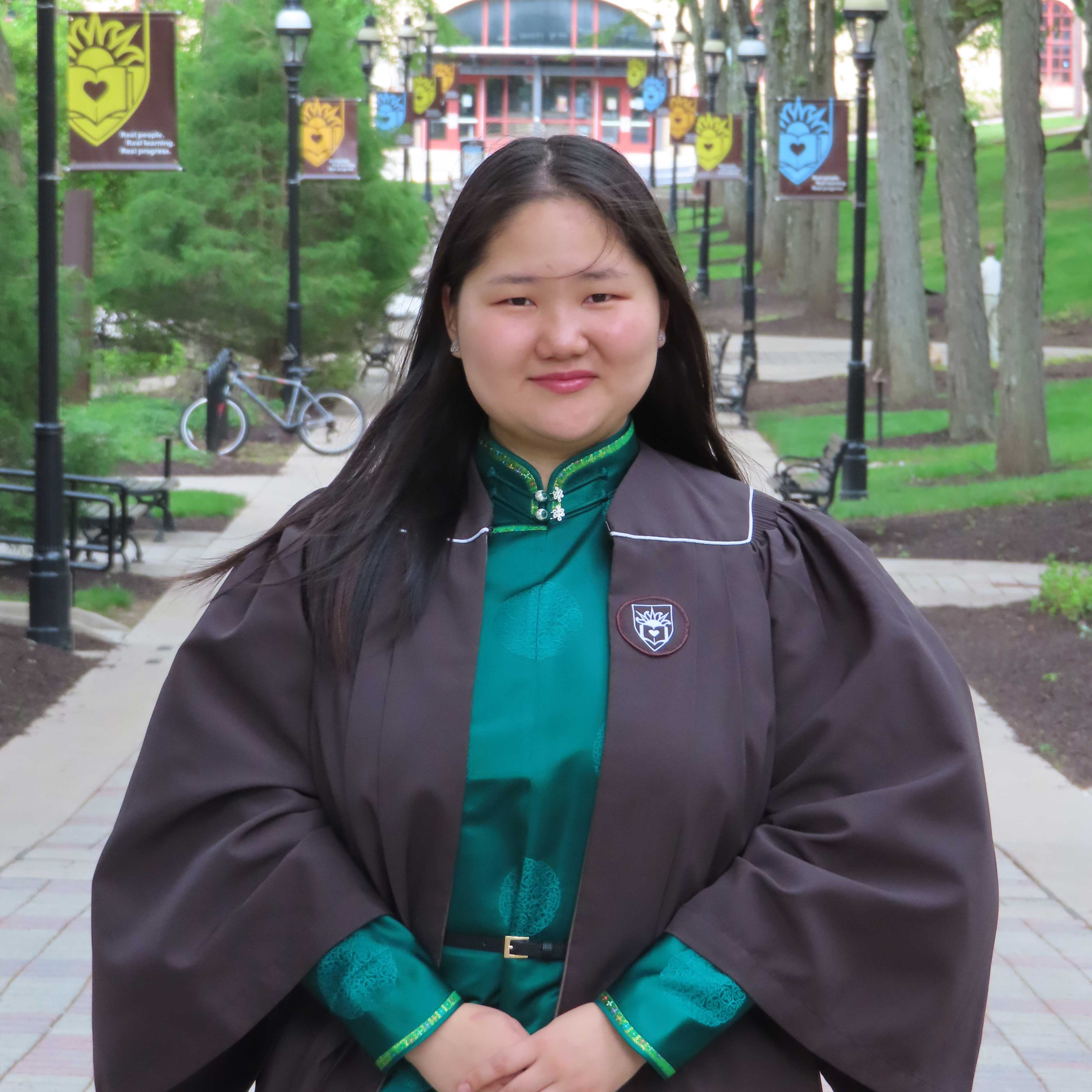 Oyu-Erdene wears her graduation gown over a green top while smiling on campus.