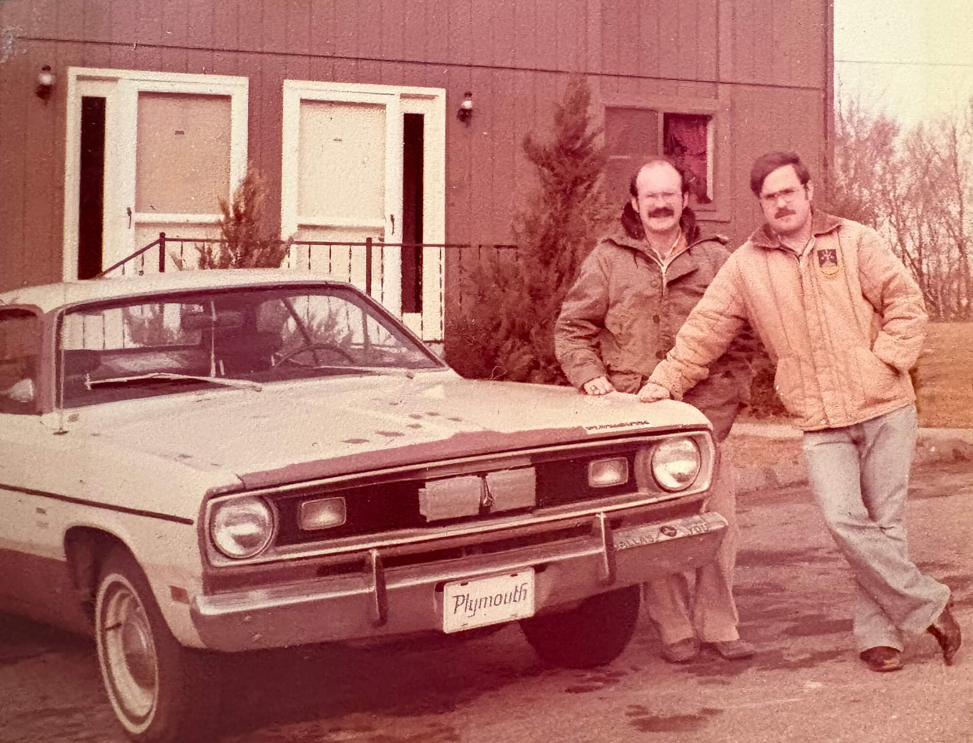 Paul Elosge stands with another man next to a vintage car in a sepia-tones photograph.