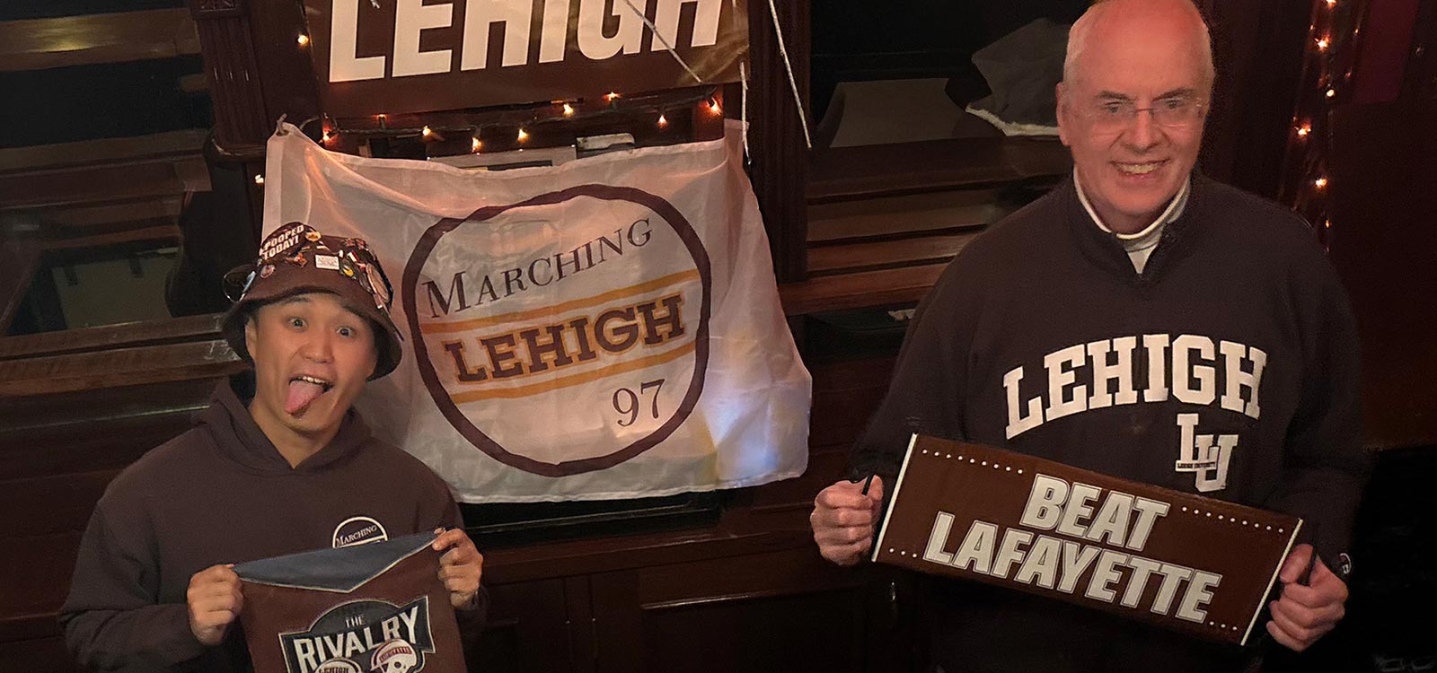  Kal and Evan smile and hold ‘Beat Lafayette’ signage while wearing Lehigh gear from head-to-toe.