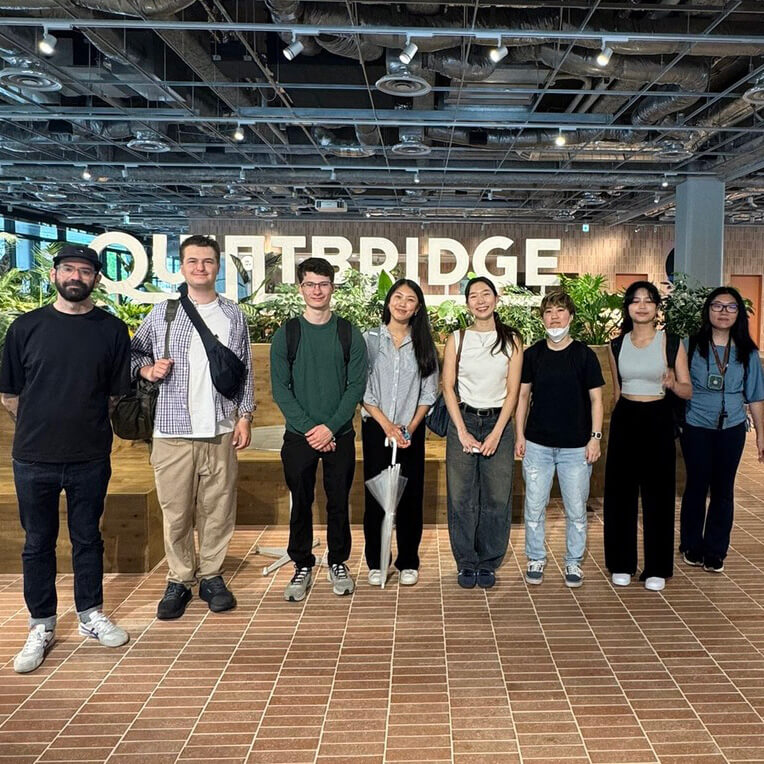 Eight students stand alongside each other for a photo in an industrial office space.
