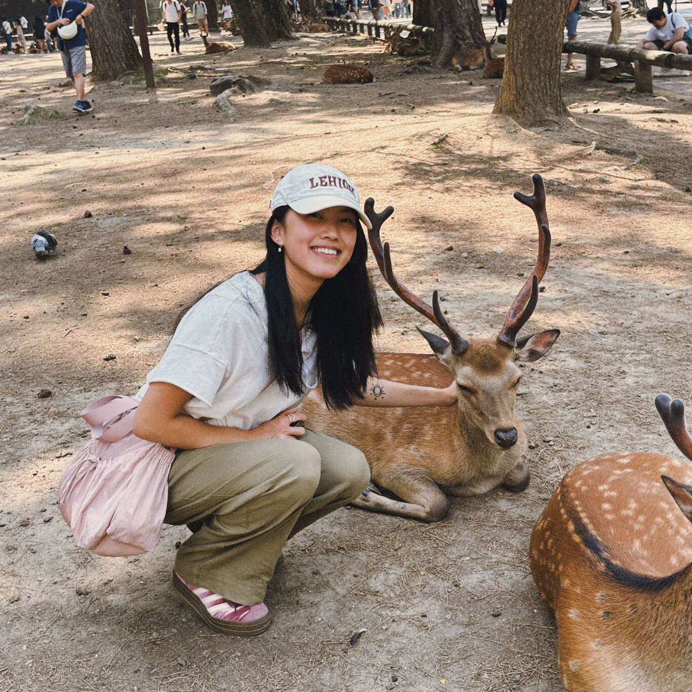 Ava DeLauro squats down beside a deer with antlers and smiles at the camera. 