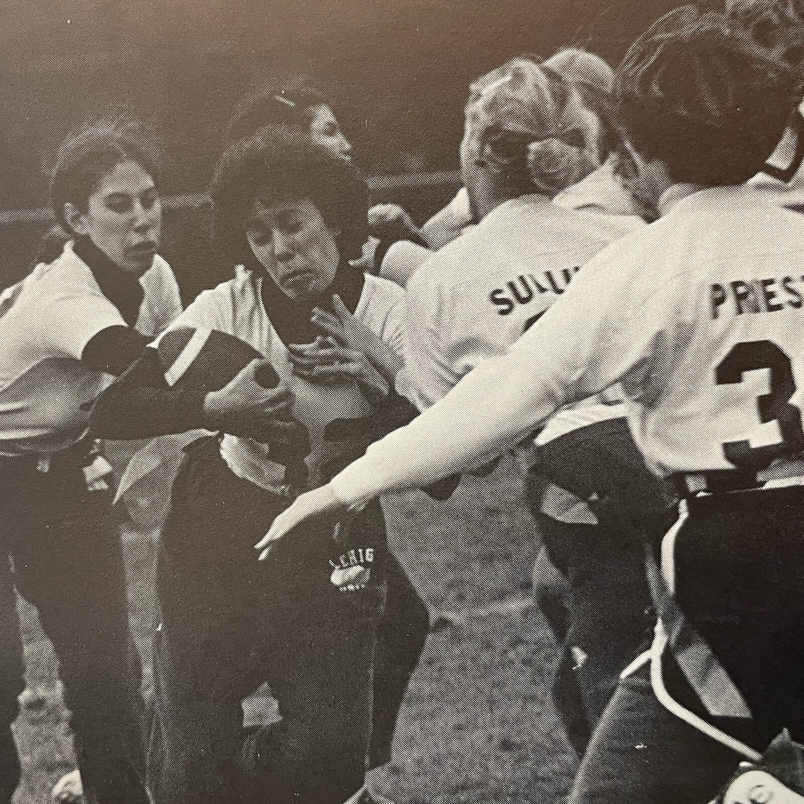 A group of female football players collide on the field with one woman holding the ball grimacing as she weaves through the crowd.