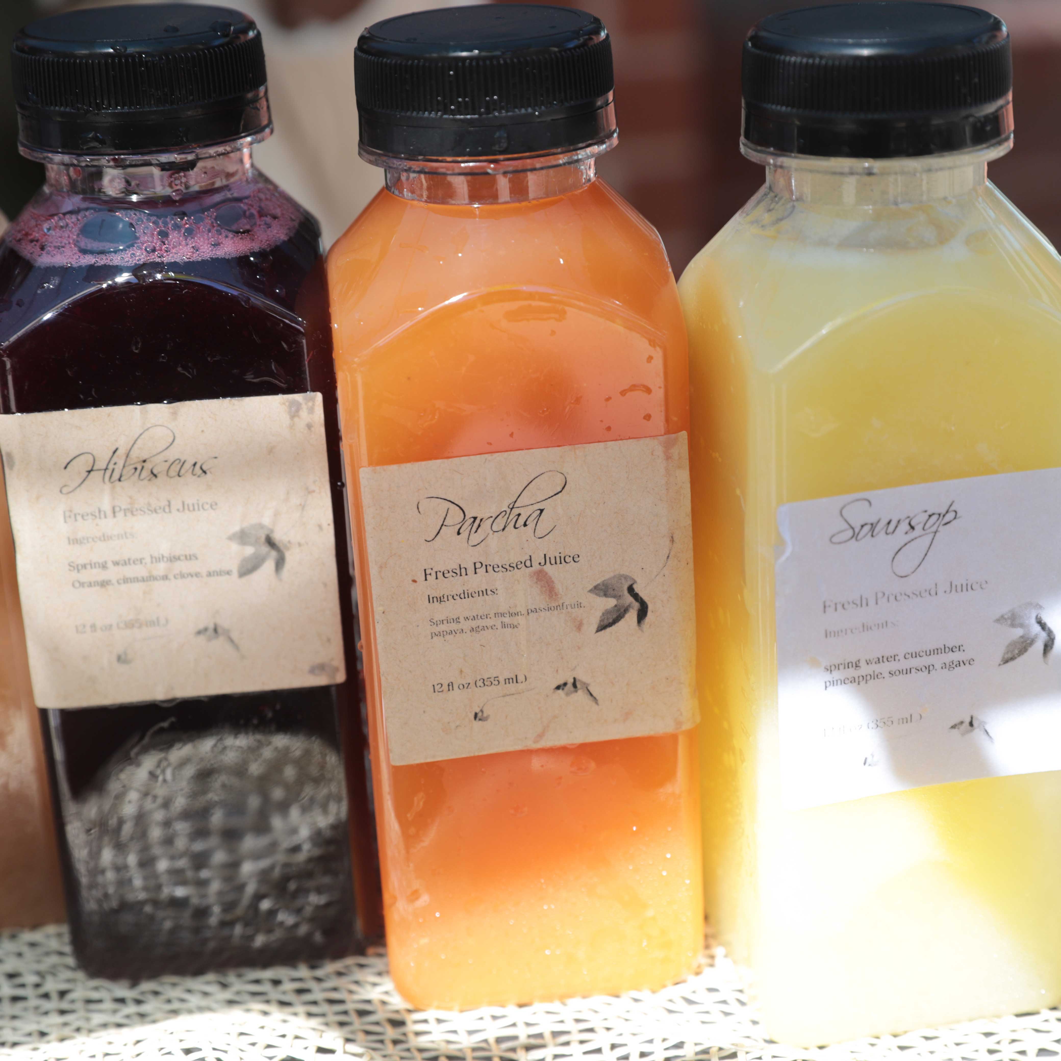 Three bottles of labeled, vibrant-colored juice including hibiscus, parcha, and soursop. 
