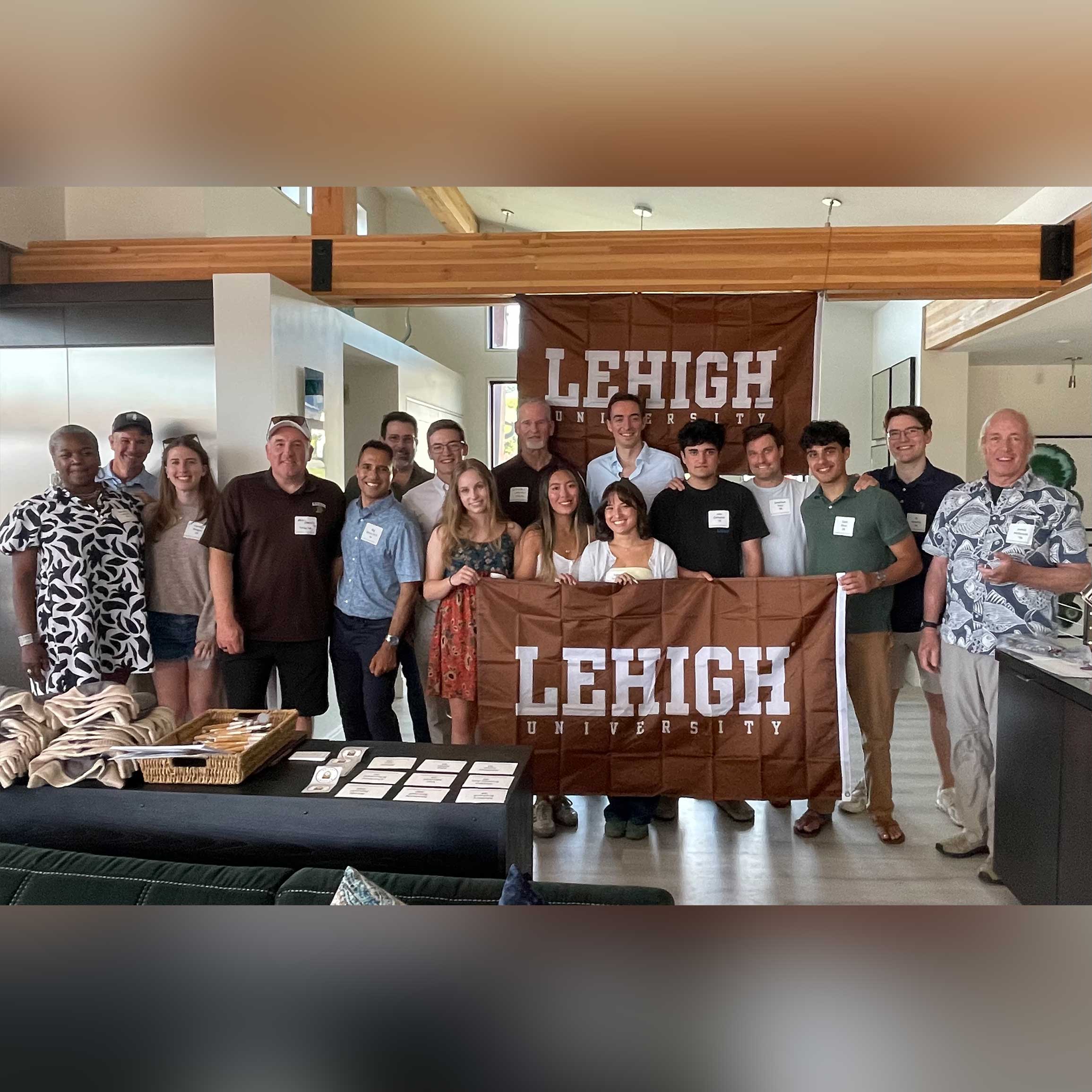 A group of students, alumni, and their families stand together and smile while holding a Lehigh banner. Raj stands with them.