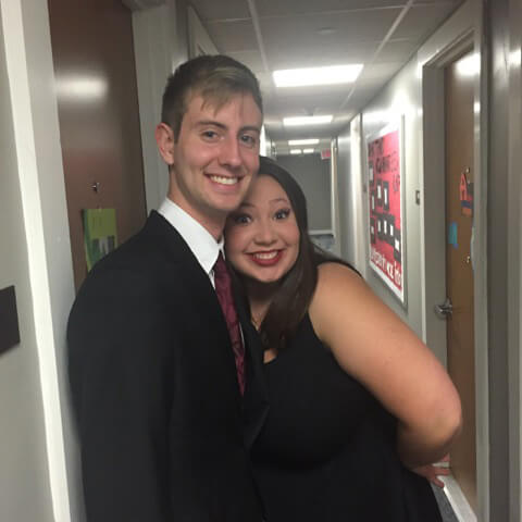 In a hallway and dressed in semi formal garb, Sara Anderson and Christian Hillegas pose smiling with Sara’s head on Christian’s chest.