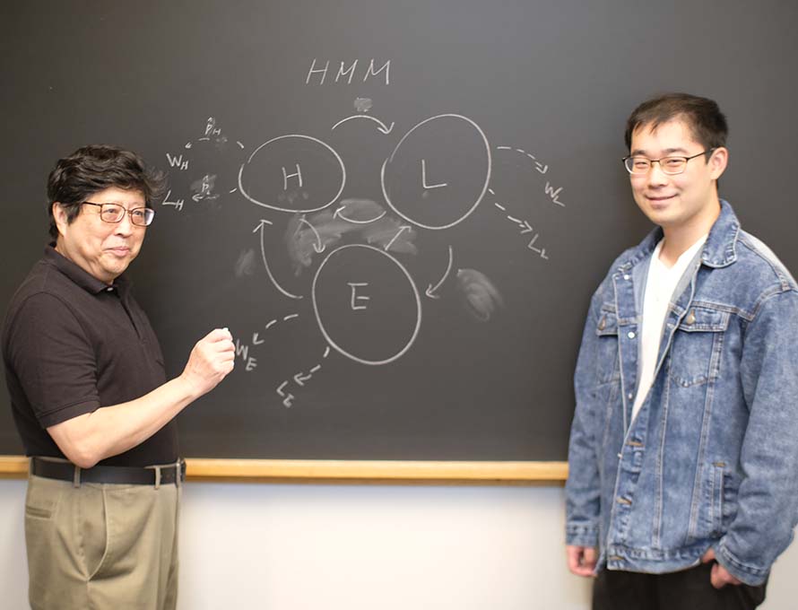 Professor and student stand in front of math diagram on chalk board
