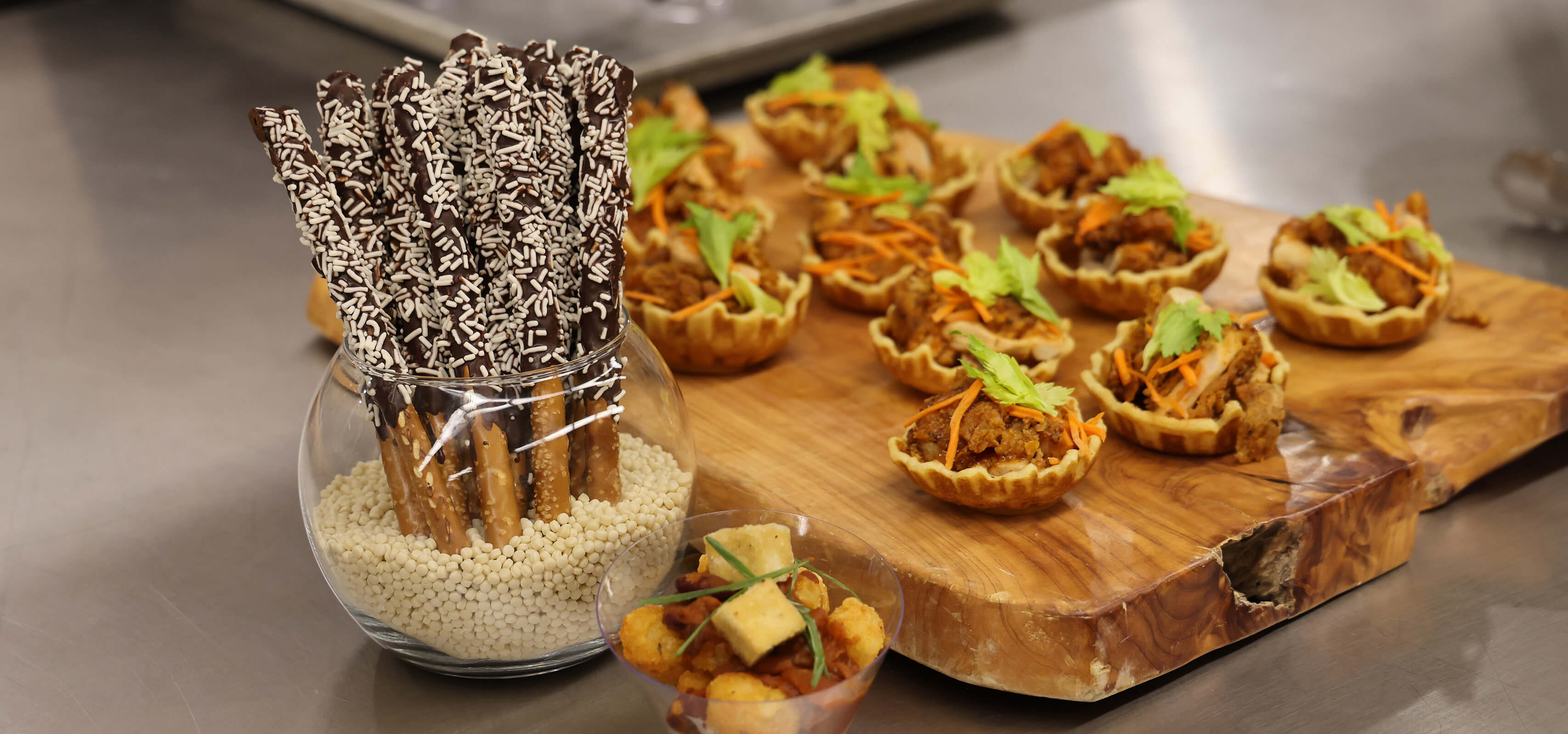 A fish bowl-style vessel holds roughly 10 chocolate dipped pretzel rods, placed beside other appetizer-style munchies.