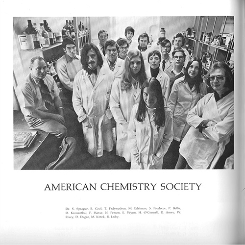 Ron stands among a large number of students in lab jackets